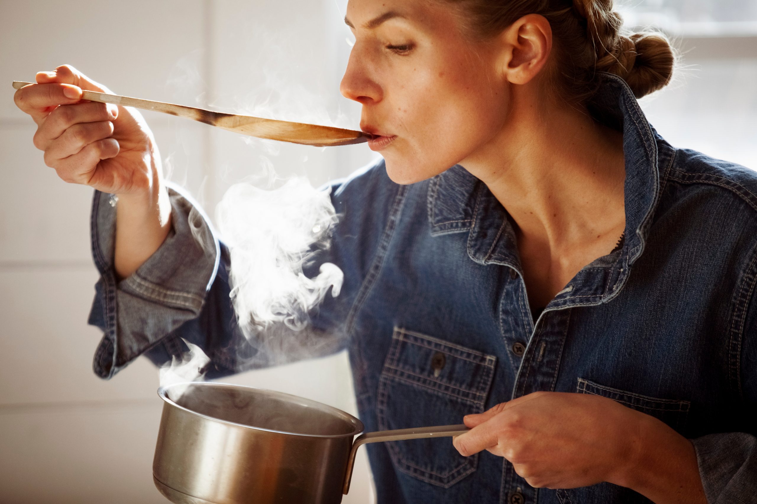 Woman tasting food while standing in kitchen at home